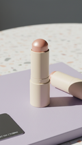 Multi-use skin highlighter stick, Three-quarter product angle on matte pastel surfaces (lilac or peach), shot in diffuse...